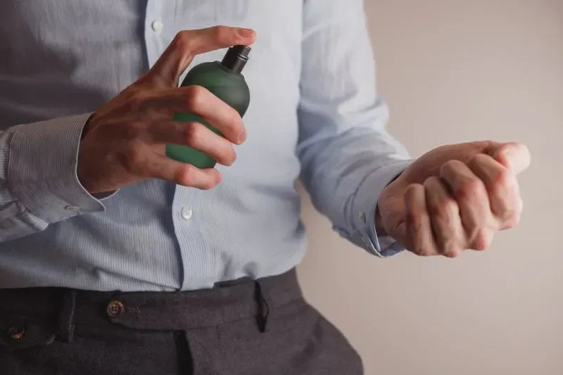 A man spraying office perfume on his wrist while dressed in a formal shirt, preparing for the day with a refined fragrance.