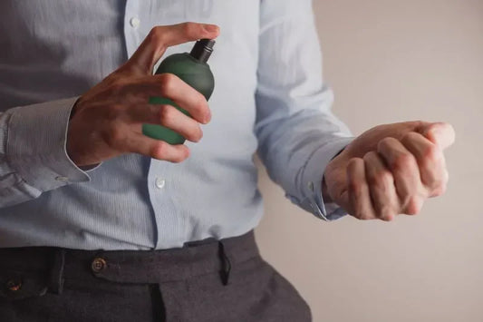A man spraying office perfume on his wrist while dressed in a formal shirt, preparing for the day with a refined fragrance.