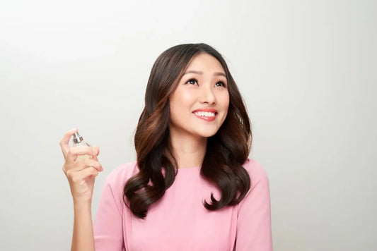 A woman smiling while holding a bottle of the best smelling perfume for women, demonstrating the joy and elegance of wearing a premium fragrance